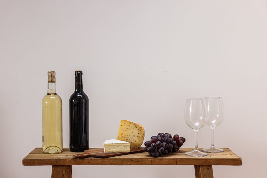 A rustic setting with wine, cheese, grapes, and wine glasses on a wooden table.